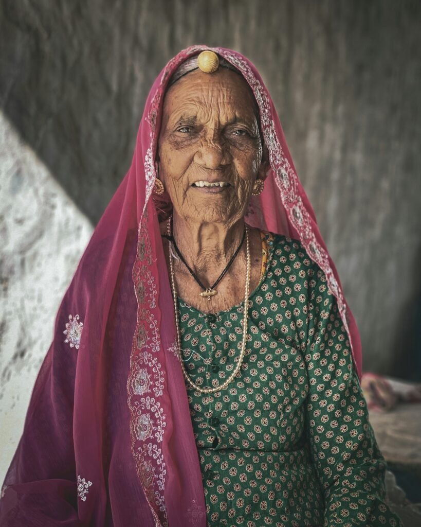 An elderly woman in a green and pink sari
